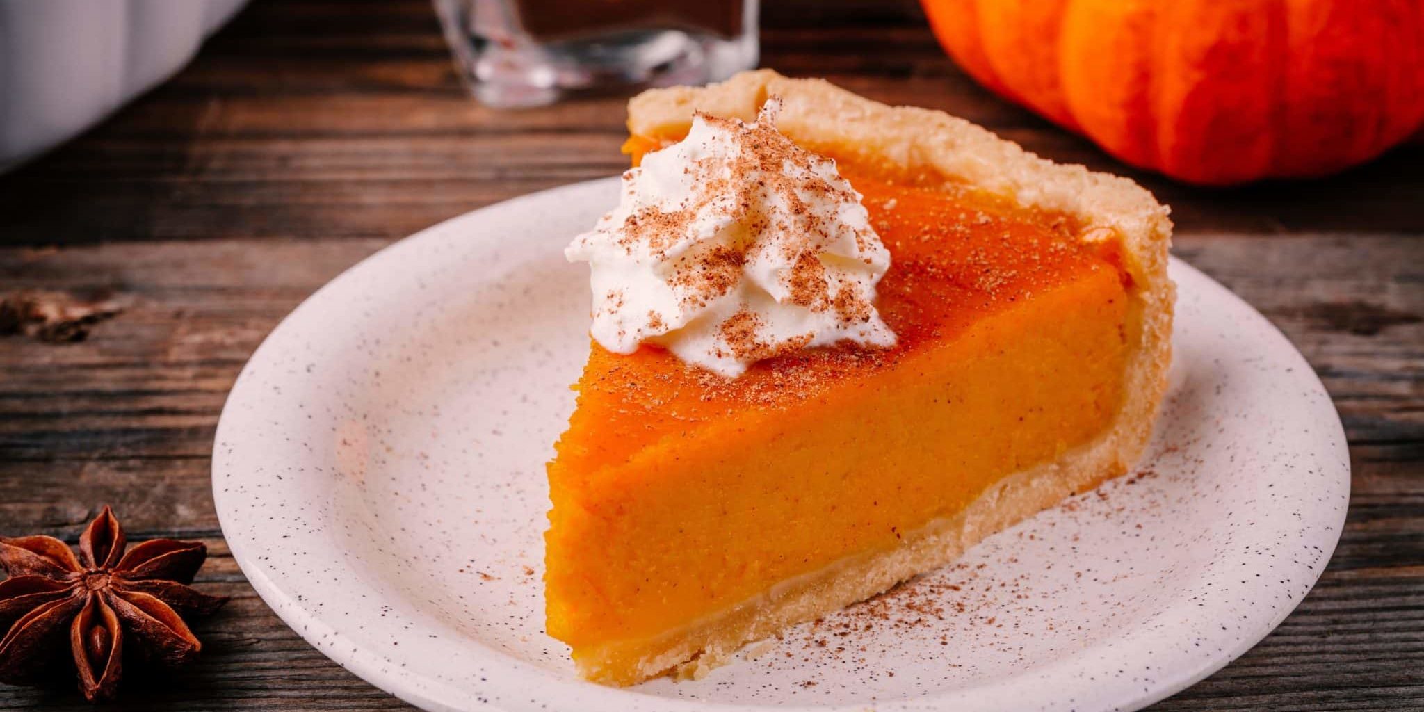 Homemade Pumpkin Pie for Thanksgiving with whipped cream and cinnamon on wooden background