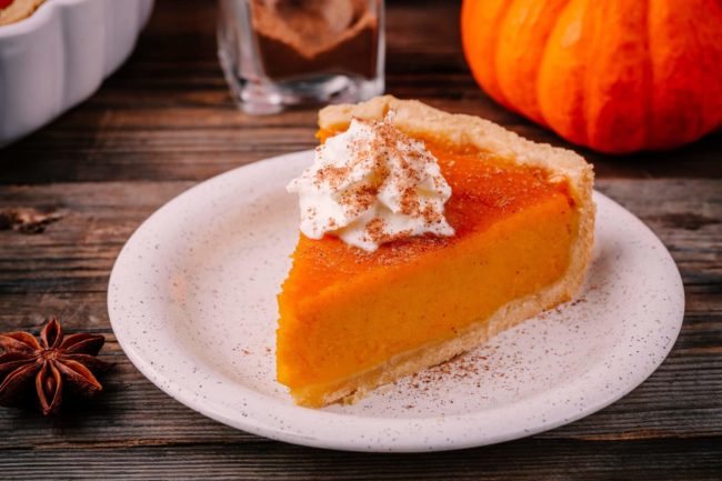 Homemade Pumpkin Pie for Thanksgiving with whipped cream and cinnamon on wooden background